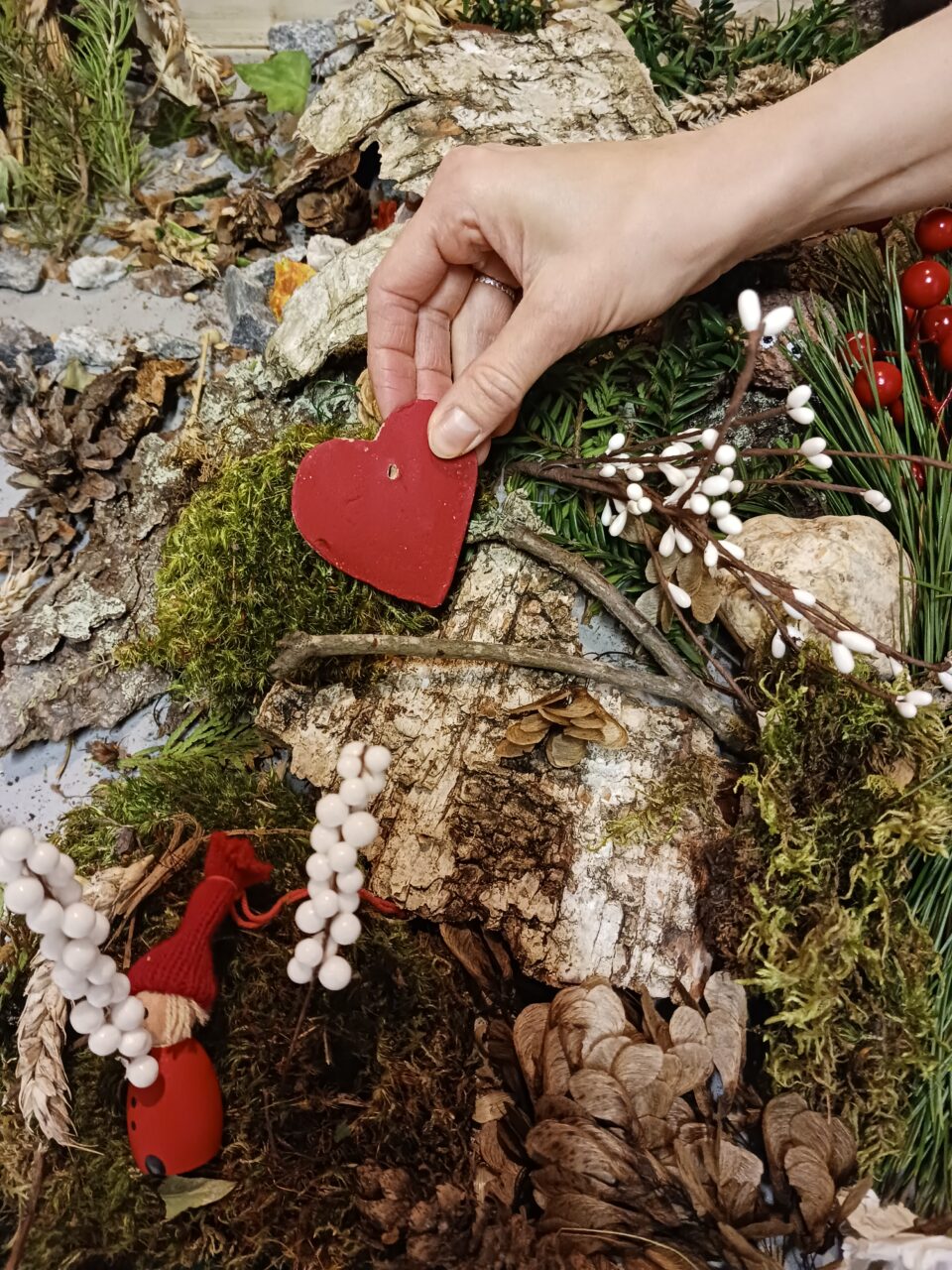 Kädessä huovutettu sydän sammaleen ja kaarnan keskellä.