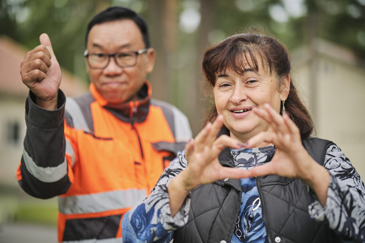 Diakonkylässä kaksi ihmistä, toinen tekee käsillään sydämen ja toinen näyttää peukkua.