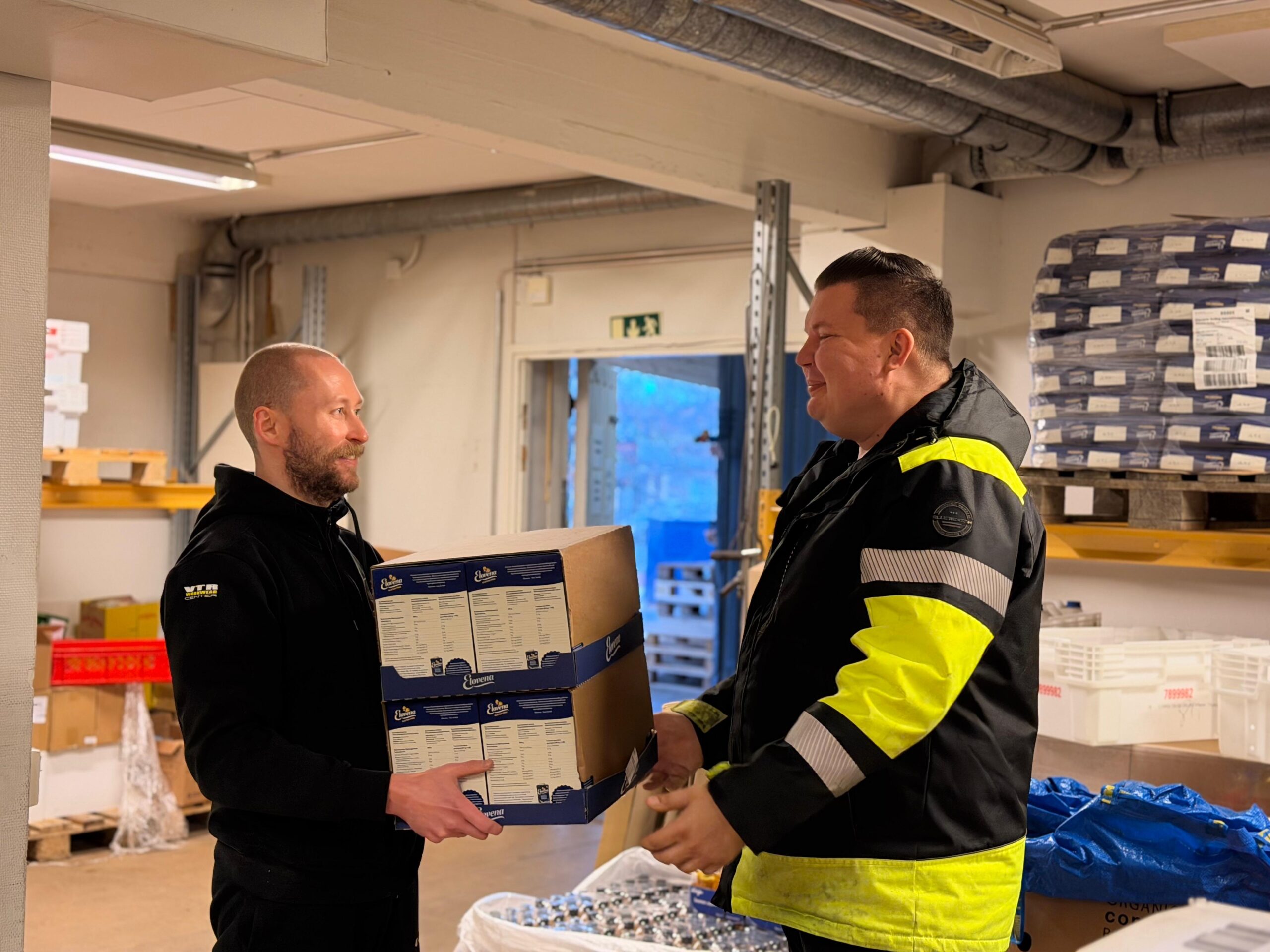Työntekijä ojentaa ruokalaatikon toiselle varastossa.