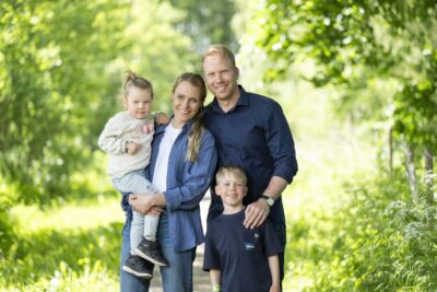 Nelihenkinen perhe seisoo vehertävän puiston keskellä