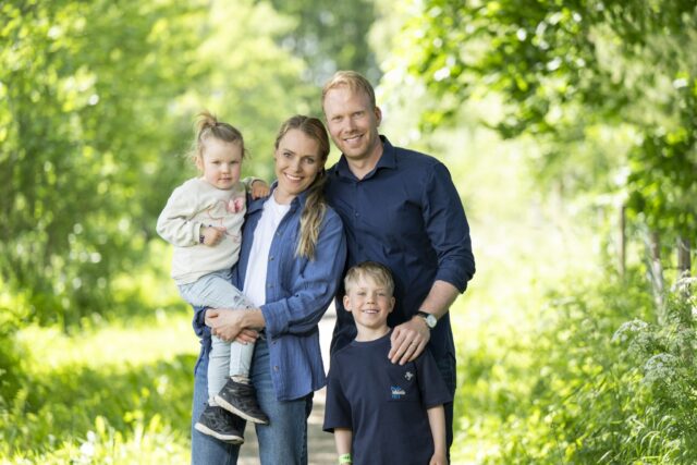 Nelihenkinen perhe seisoo vehertävän puiston keskellä